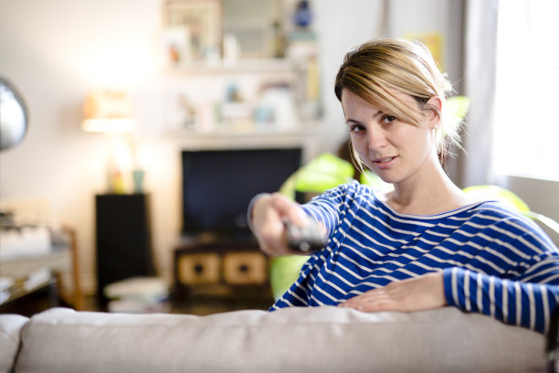 年轻漂亮的女人坐在家里的沙发上看电视图片下载