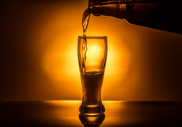 深色玻璃啤酒倒在灯光背景上，特写图片下载