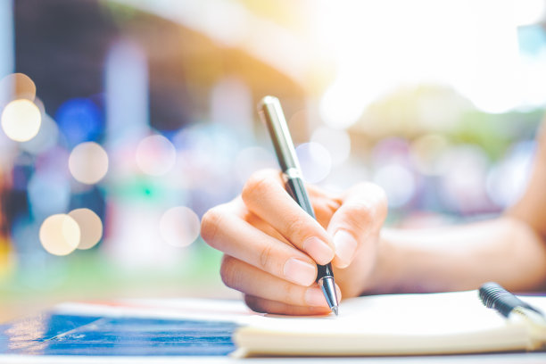 一个女人的手在木桌上用钢笔在记事本上写字。素材图片