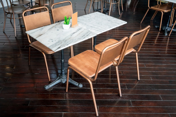 大理石餐桌与黄铜金属椅子，在黑色的木地板上用餐。素材图片