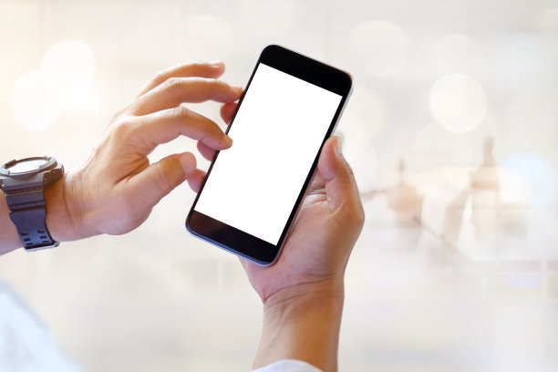 Мужчина держит в руках смартфон с пустым экраном в коворкинге или кафе.图片下载