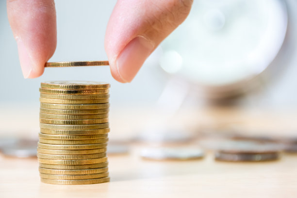 手放金币堆叠以模糊时钟为背景，金融投资省钱理念图片下载