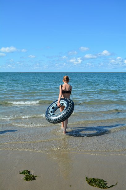 带着游泳轮胎的女孩在海滩上在海里跑图片下载