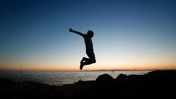 快乐的小男孩在夕阳下跳跃图片下载