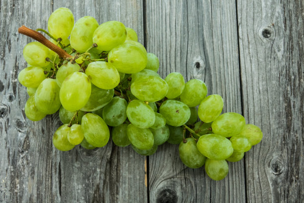 一串熟透多汁的绿葡萄在树林背景上的特写素材图片