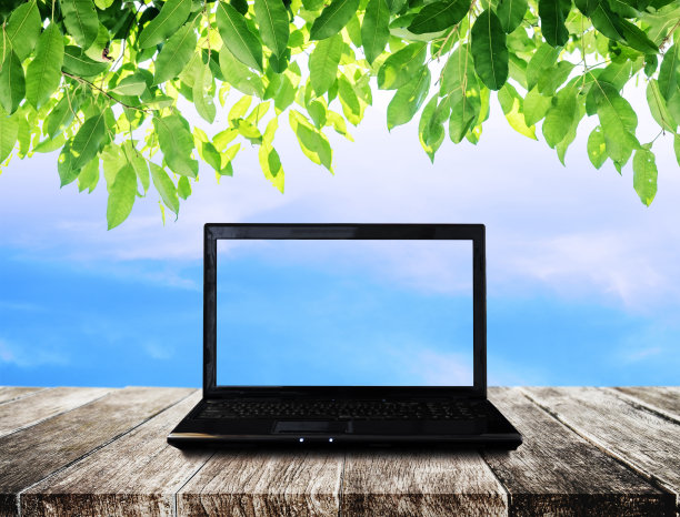 笔记本电脑放在木桌上，以蓝天绿叶为背景图片下载