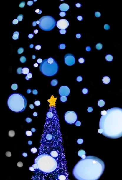 模糊的蓝色大灯和小灯散焦的圣诞装饰线挂在玻璃建筑前，用模糊的蓝色大灯和模糊的黄色星星装饰圣诞特别庆祝图片下载