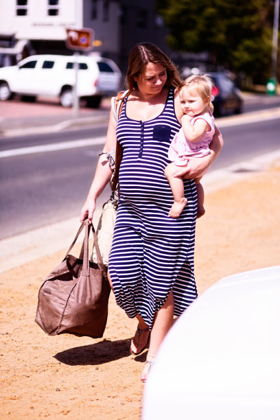 一名孕妇抱着蹒跚学步的孩子在街上购物图片下载