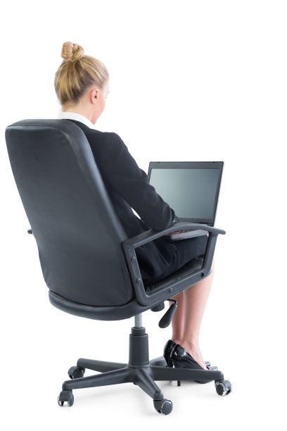 后视图的金发年轻女商人坐在办公椅上使用她的笔记本电脑图片下载