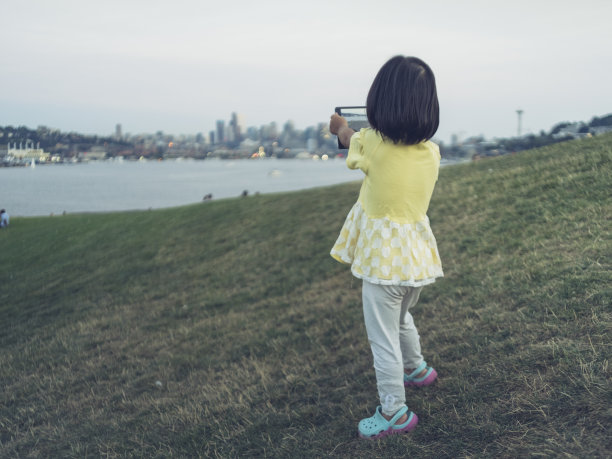 一个亚洲小女孩在草坪上用数码平板电脑拍照图片下载