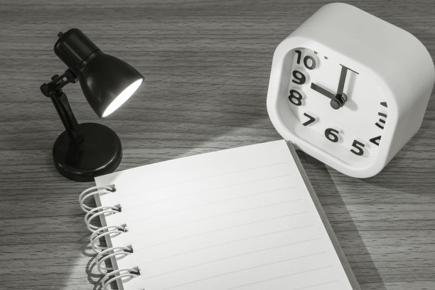 特写笔记与灯光从小灯和白色闹钟在黑暗的房间木质书桌上黑色和白色调纹理背景图片下载