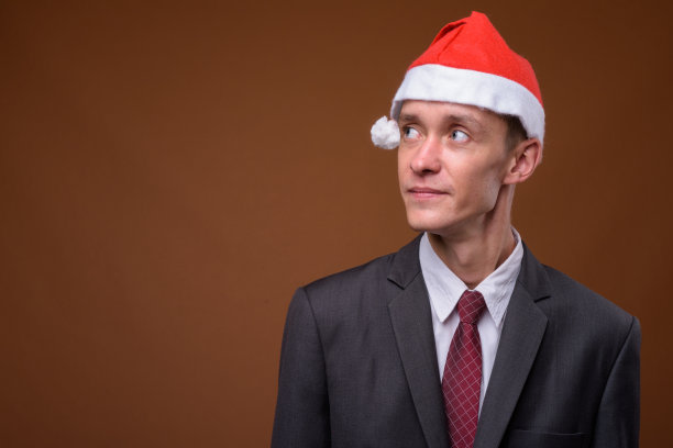 工作室拍摄的年轻商人戴着圣诞帽准备圣诞节的彩色背景图片下载