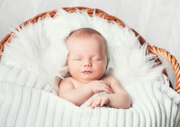熟睡的新生婴儿躺在柳条篮子里的白毯子上。图片下载