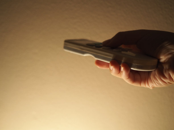 手握空调遥控器，黄澄澄的灯光，颗粒状的水泥墙面，戏剧性图片下载