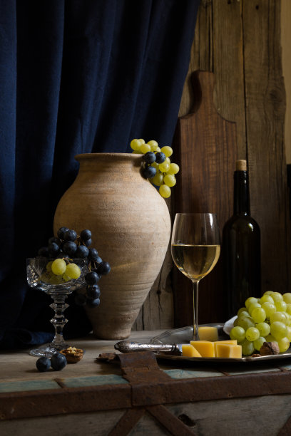 白葡萄酒在玻璃高脚杯绿黄色的葡萄，瓶子和陶罐，奶酪盘木板，复古老酒馆静物图片下载