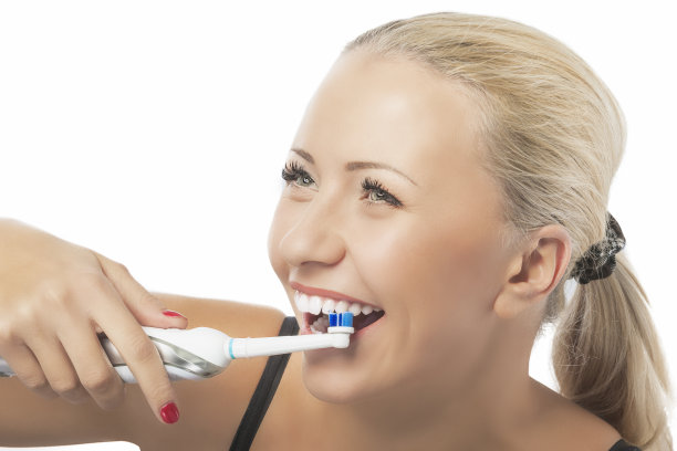 牙齿健康:白种金发女人用现代电动牙刷刷牙。素材图片