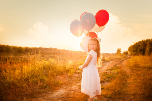 金色的夕阳下，拿着彩色气球的女孩图片下载