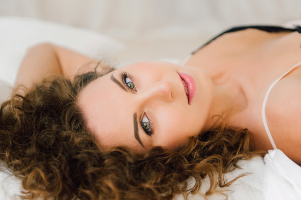 性感的女人在床上早上显示她美丽的身体。在她卧室的自然光中醒来，盖上床单。处理过的照片。图片下载