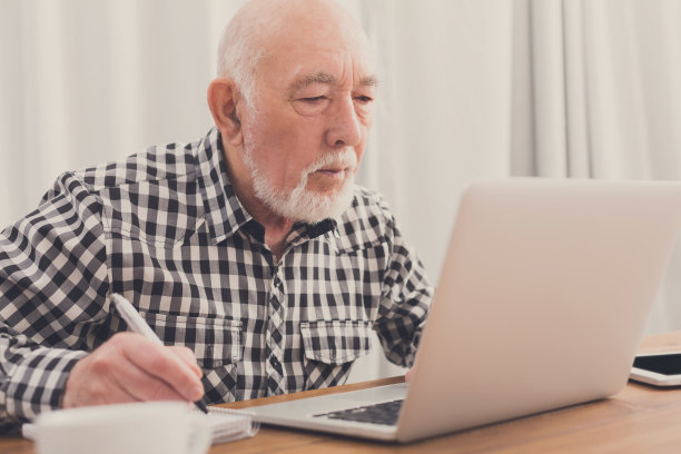 成熟的男人使用笔记本电脑，在记事本上写字图片下载