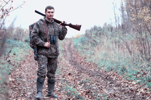 一名身穿迷彩服，手持猎枪的男子在森林里图片下载