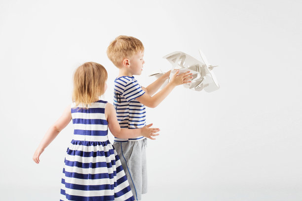 孩子们坐在地板上玩纸玩具飞机，背景是白色。图片下载