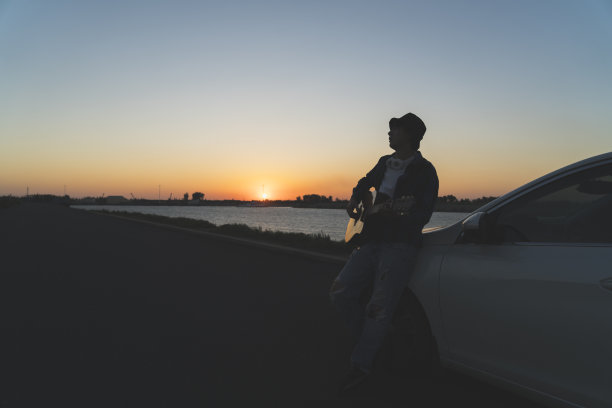 年轻男子靠在汽车引擎盖上弹吉他图片下载