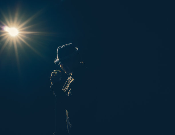 亚洲音乐家唱歌与麦克风在黑色背景与聚光灯和镜头光晕，音乐的概念图片下载