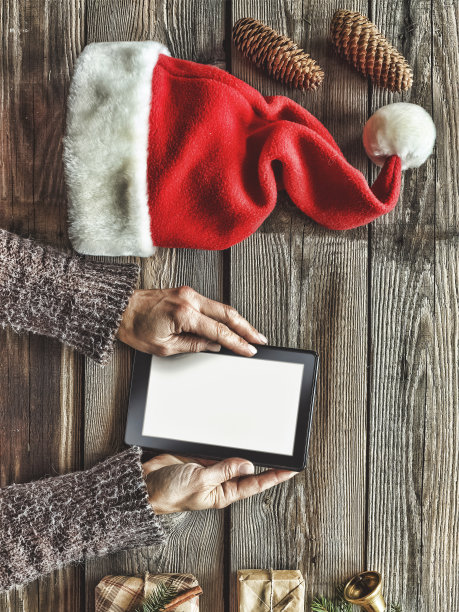 人类手中的平板电脑。桌子旁边放着平板电脑礼盒、圣诞钟声和蓬松的冷杉树枝。文本的空闲空间。前视图。副本的空间。图片下载