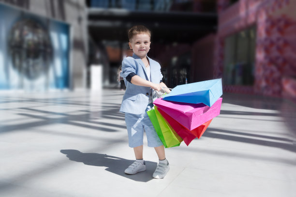 快乐的小男孩拿着购物袋走来走去。孩子在购物中心附近玩耍。图片下载
