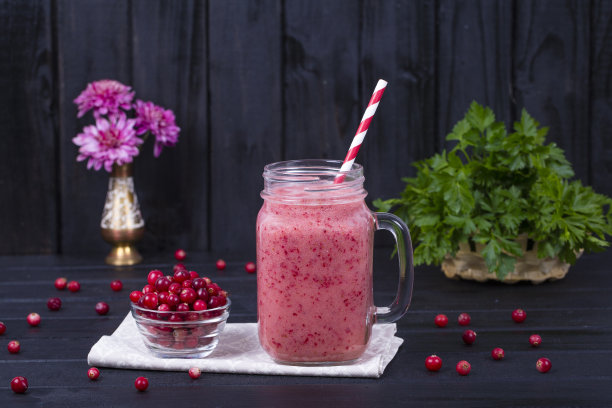 蔓越莓果汁奶昔在玻璃杯和生蔓越莓在黑色的木制背景，近距离图片下载