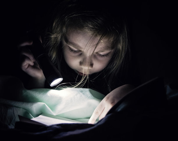 女孩用手电筒在床上看书图片下载
