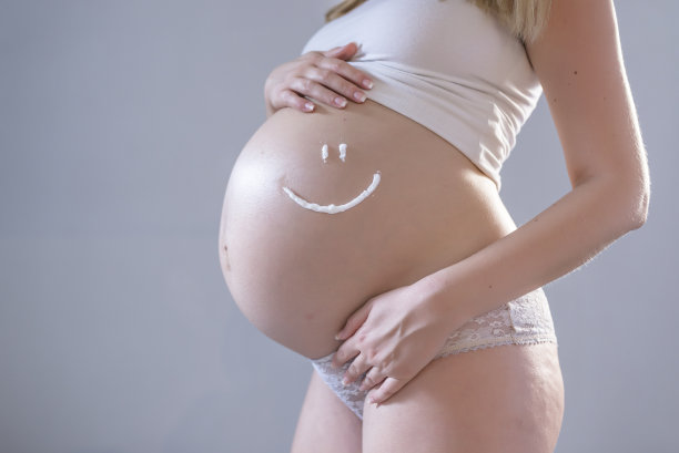 孕妇使用护理霜。年轻的孕妇使用化妆品。孕妇将面霜涂在腹部以避免妊娠纹图片下载