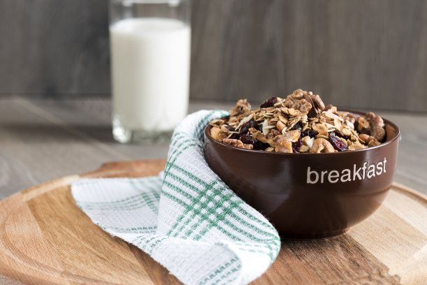 自制格兰诺拉麦片，用蜂蜜，燕麦片，腰果，杏仁，开心果，葡萄干和蔓越莓放在粘土碗里，玻璃和牛奶放在木桌上，素材图片