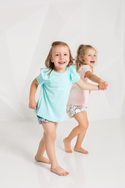 两个可爱的小女孩，穿着相同的衣服，但颜色不同，在白色的演播室里玩耍图片下载