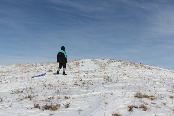冬天，穿着黑色夹克的人用塑料雪橇爬山图片下载