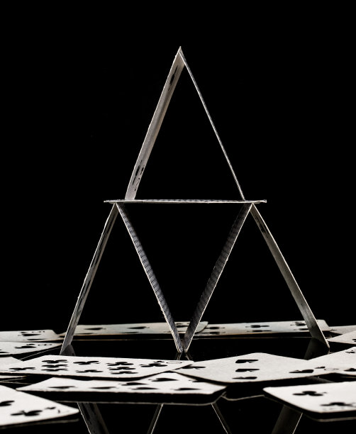 纸牌屋由白色扑克牌组成，正面拍摄，有反射，表面散落散落的纸牌，黑色背景图片下载