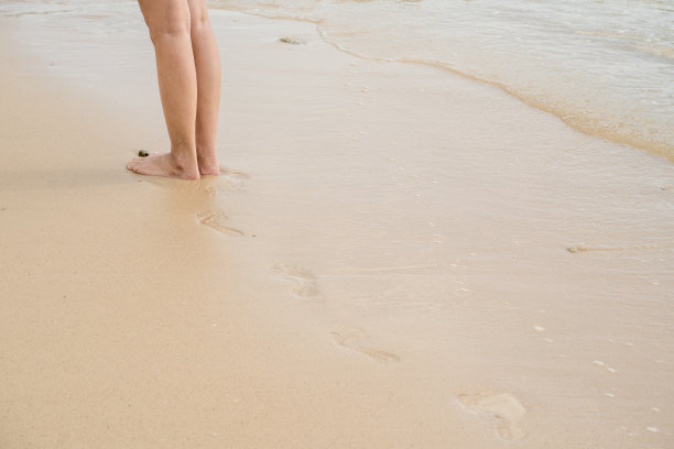 女人走在沙滩上，脚印在沙滩纹理上，复制空间。图片下载