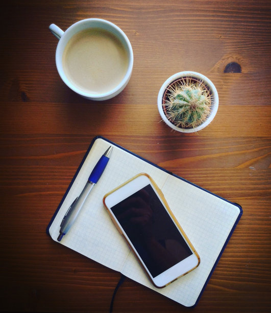 白板笔记本，木桌上放着钢笔、智能手机、仙人掌和咖啡图片下载