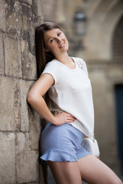 年轻女子靠在古老的石墙上休息图片下载