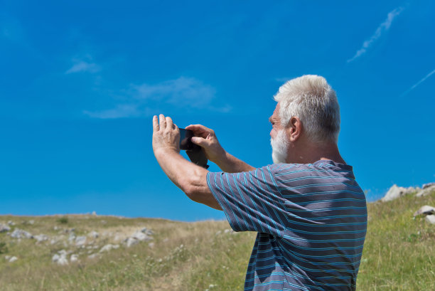 一位白胡子的退休老人正在用手机拍照。图片下载