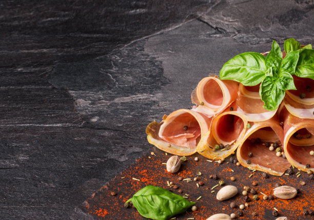 特写图片红色扭曲的火腿，罗勒叶和坚果在一个深灰色的石头背景。副本的空间。图片下载