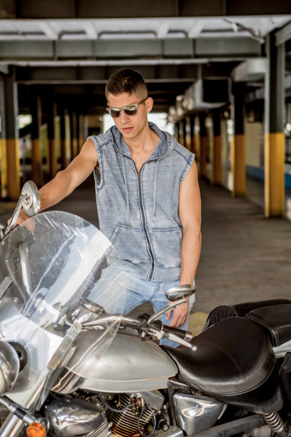 一个年轻人站在他的摩托车旁图片下载