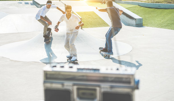 年轻的溜冰者表演与滑板和听音乐在城市公园-运动的家伙表演的技巧和技能在日落-极限运动和友谊概念-温暖的复古滤镜图片下载