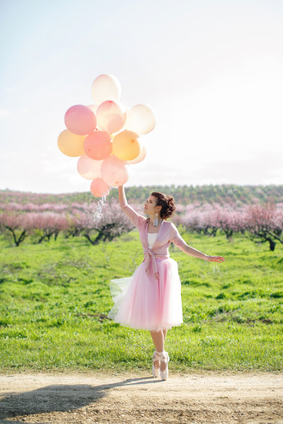 美丽的女人，在一个鲜花盛开的春天的花园里，拿着粉色的气球图片下载