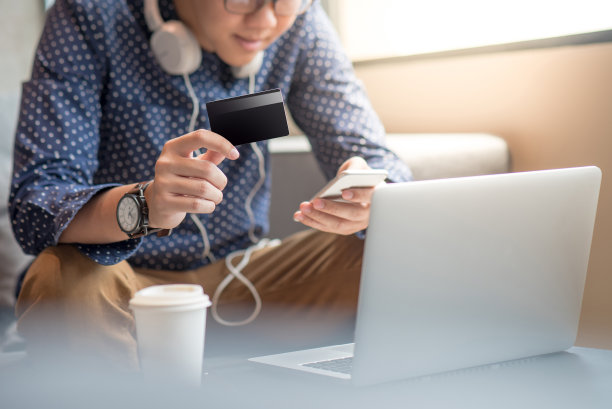 年轻的亚洲男子持有信用卡并使用智能手机进行网上购物图片下载