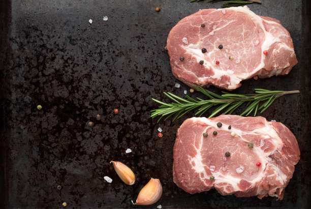 两份生猪肉排放在黑色的乡村金属烤盘上，加入迷迭香和香料。图片下载