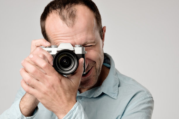 一名身穿蓝色t恤的成熟白人男子正在学习如何使用数码相机图片下载