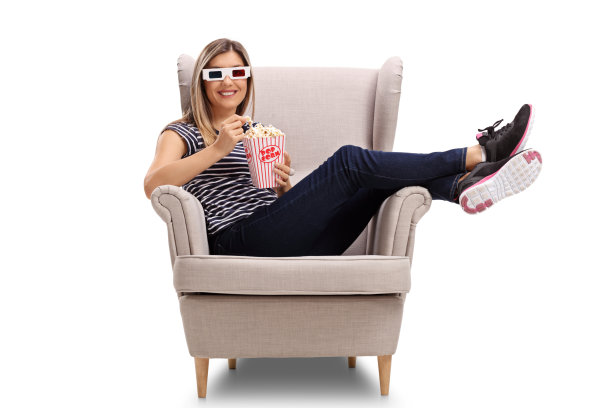 年轻女子戴着3D眼镜，吃着爆米花坐在扶手椅上图片下载