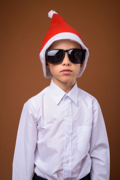 在彩色背景下，小男孩扮成商人戴着圣诞帽准备迎接圣诞节图片下载