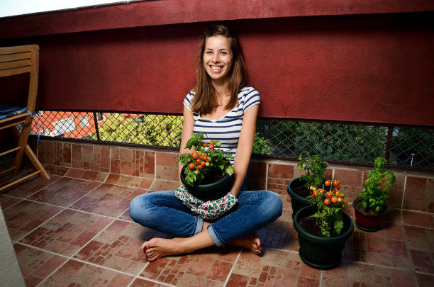 美丽的年轻女子的肖像抱着自家种植的樱桃西红柿在她的阳台上。素材图片